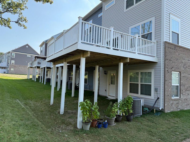 Townhouse exterior back view with tall elevated white deck and gray vinyl siding
