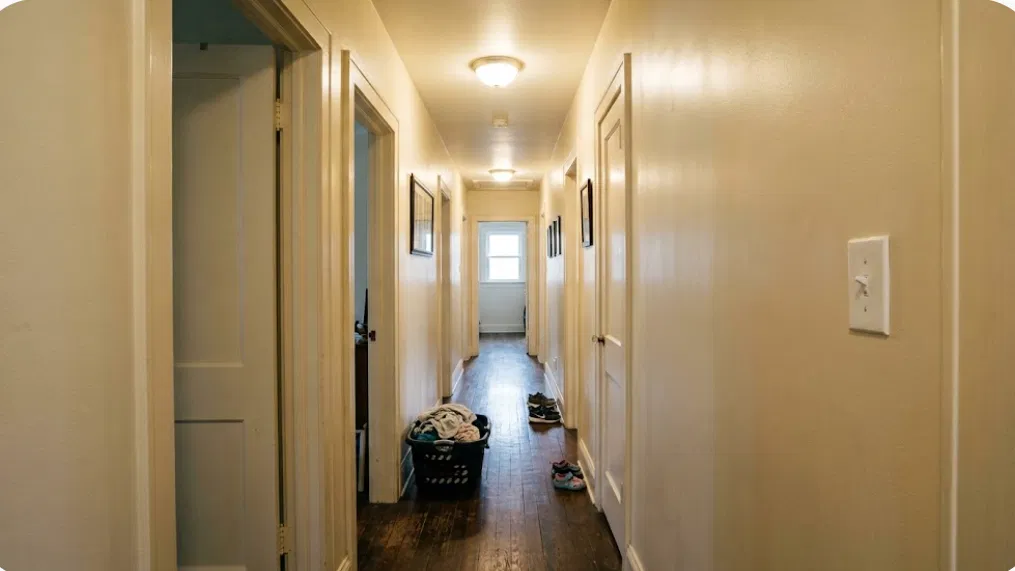Long hallway with warm satin-finish walls, several doors, and hardwood floor catching soft light