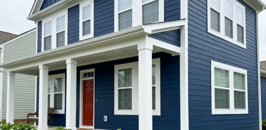Two-story house with navy blue siding, white trim and porch columns, a red front door and hydrangeas along the porc