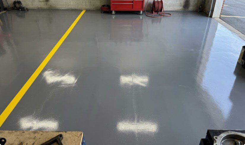 Glossy gray epoxy floor with a yellow safety line in an auto service bay