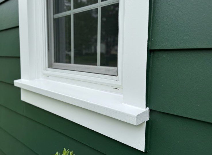 A white window sill and trim repainted smooth on a house with green lap siding, with no peeling at the corner
