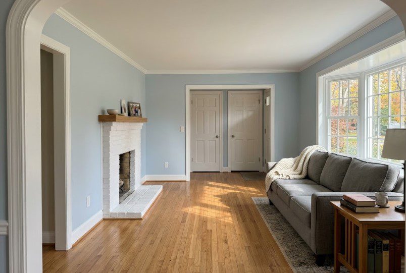 Freshly painted light blue living room with white trim, a white-painted brick fireplace and hardwood floors